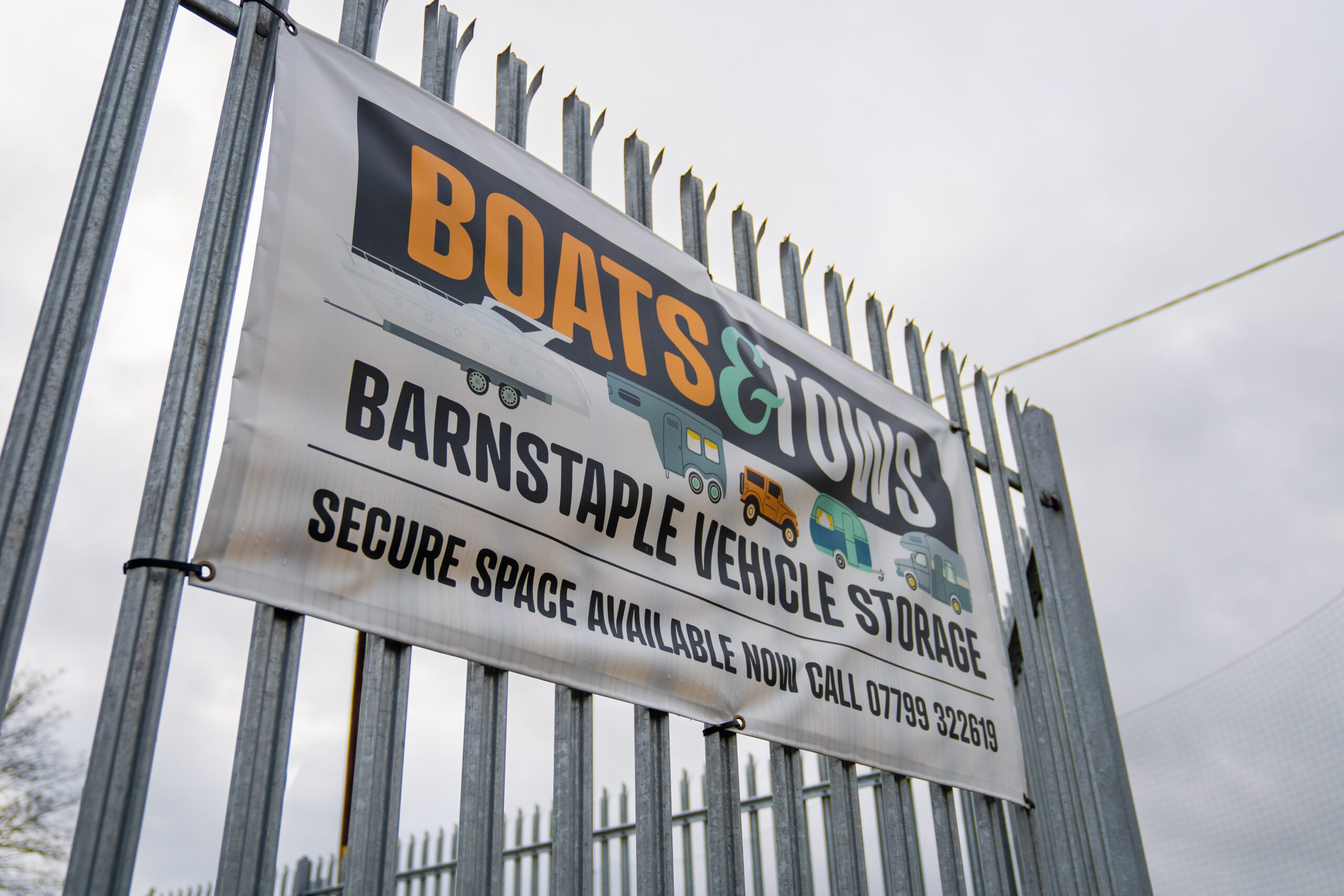 Security fencing with a banner on it reading 'Boats & Tows Barnstaple Vehicle Storage'